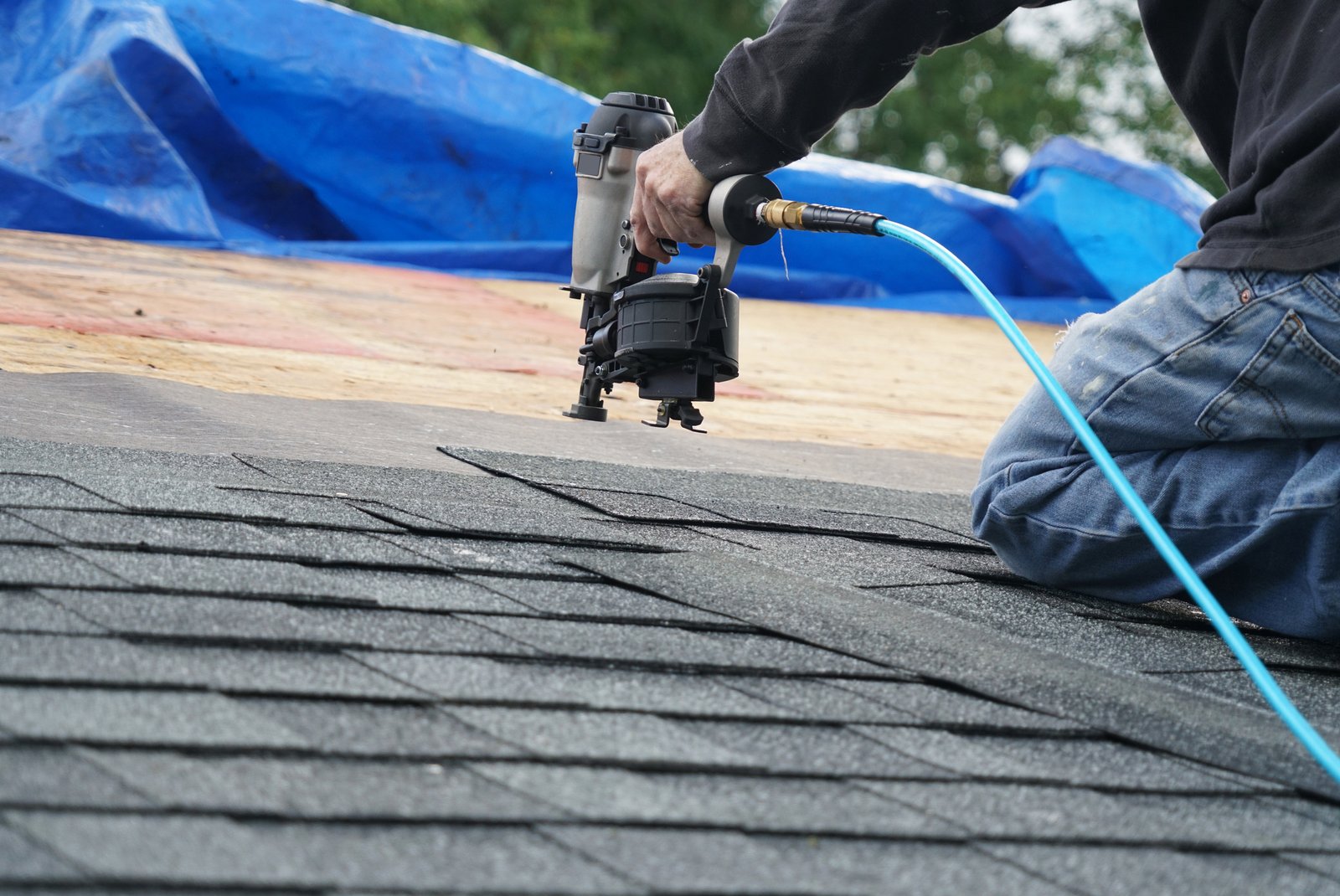 Roofer using a nail gun to install asphalt shingles on a residential roof