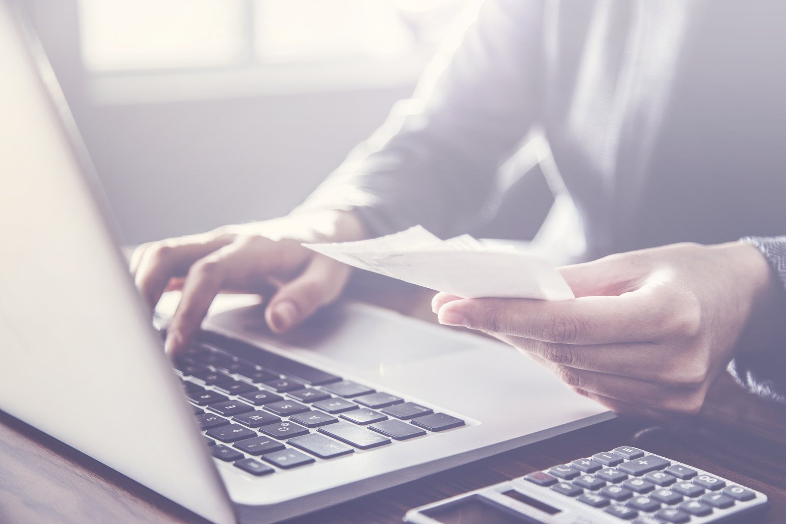 Hands typing on a laptop while reviewing job paperwork at a desk