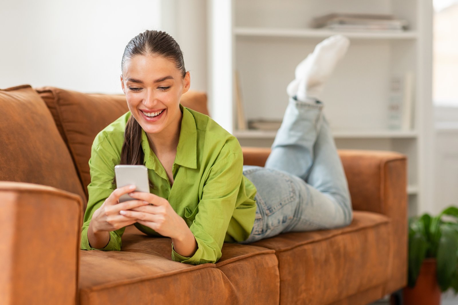 Homeowner relaxing on a couch while booking a service appointment on her phone